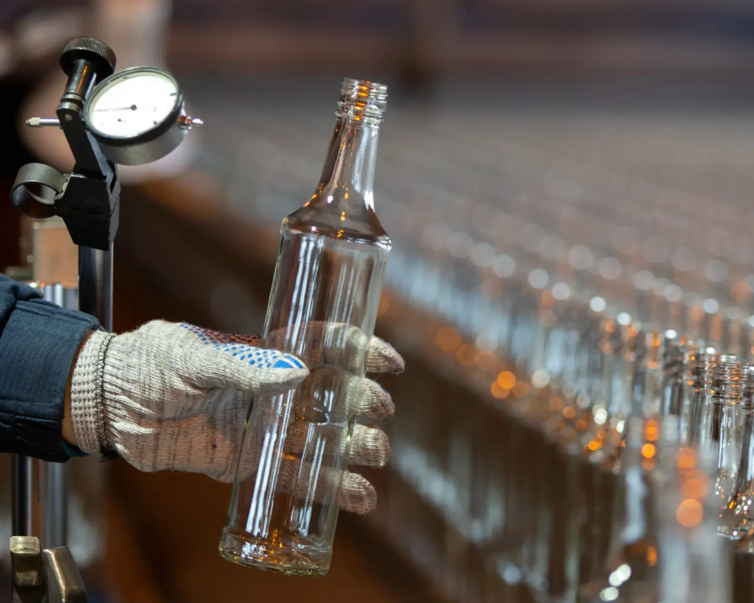 Eine Hand mit Arbeitshandschuhen hält eine gerade produzierte Glasflasche – Symbolbild für den PCF